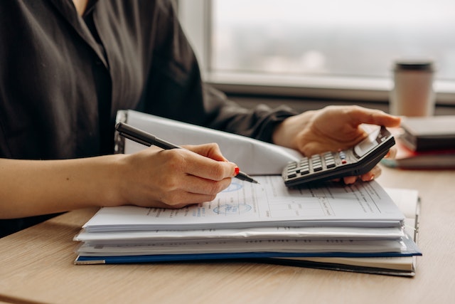 mujer revisando documentos sobre una mesa con una calculadora en la mano